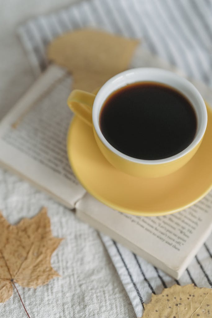 From above freshly brewed black coffee in yellow cup placed on opened book in light room